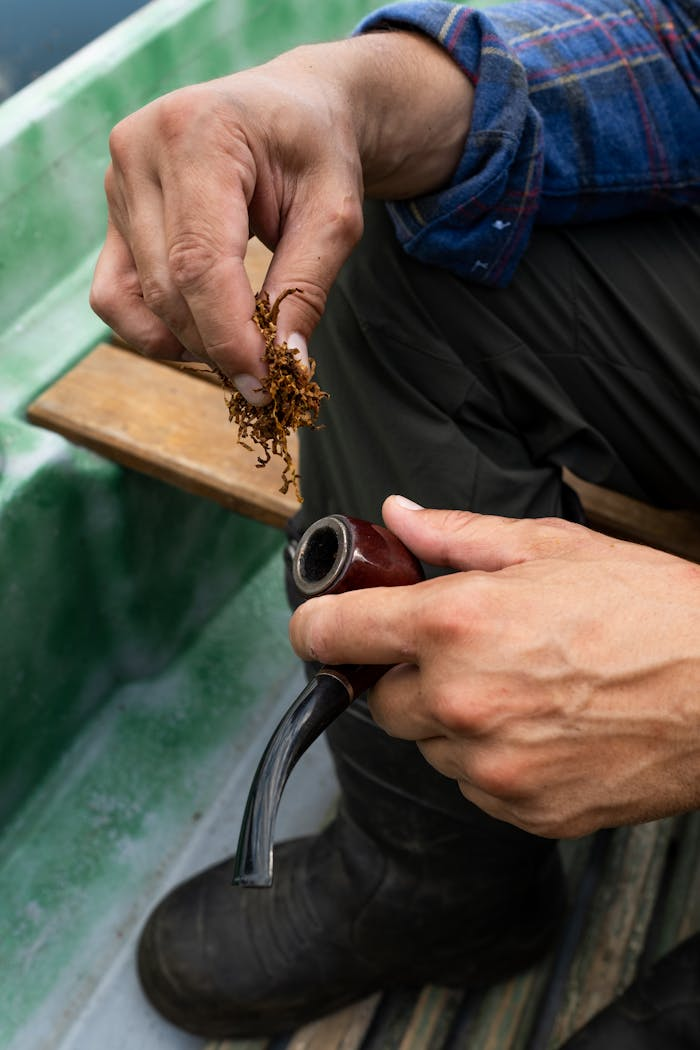 Close-up of a man preparing tobacco for a pipe on a boat outdoors.