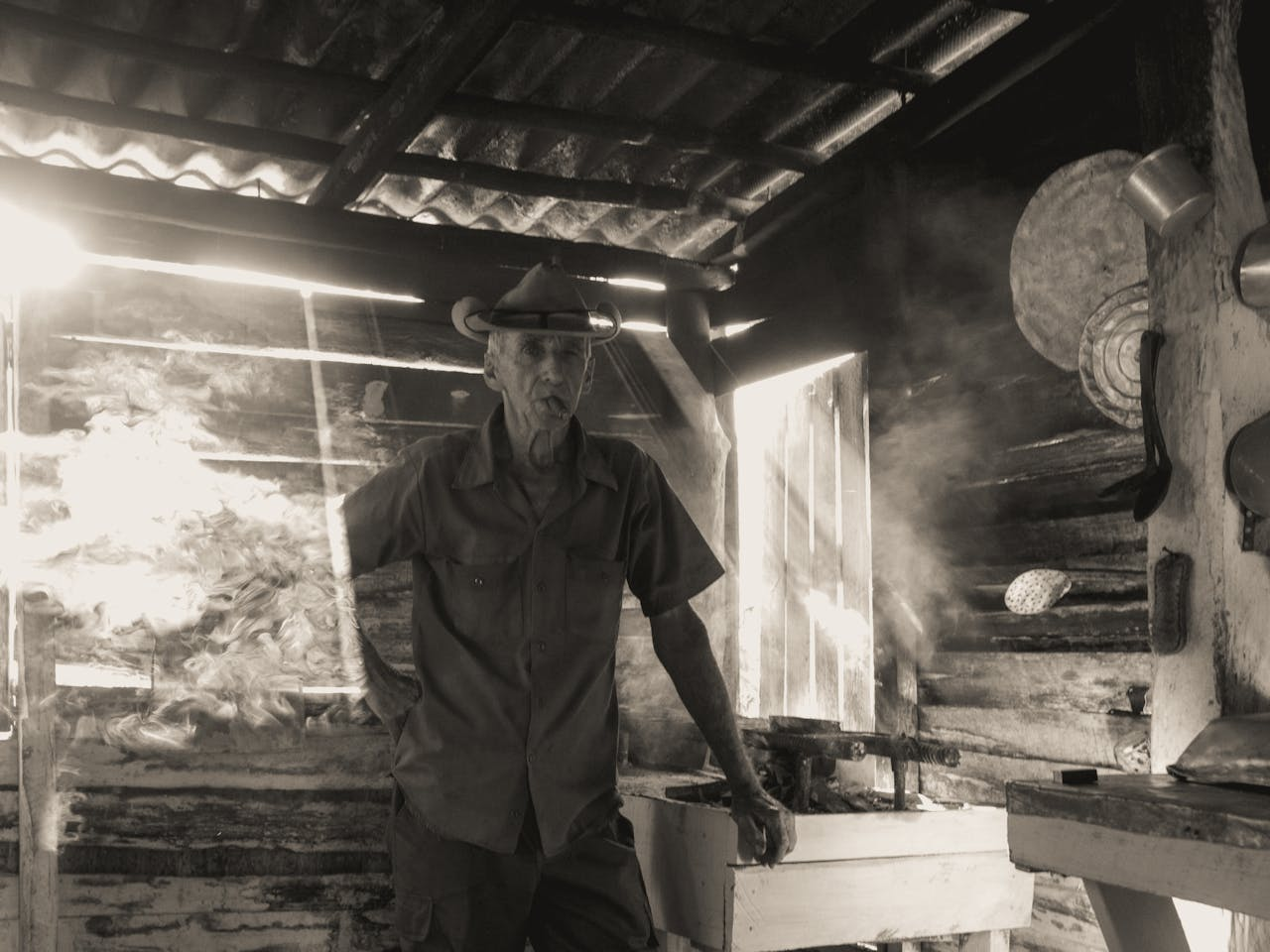 Black and white photo of an elderly man in a wooden cabin, smoking.