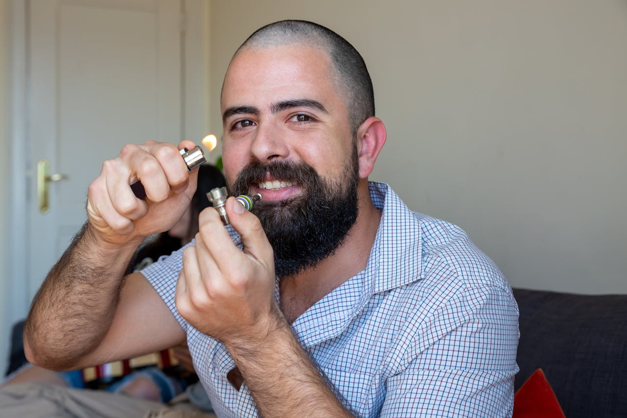 Bearded man lighting a pipe indoors, showcasing lifestyle and relaxation in Portugal.