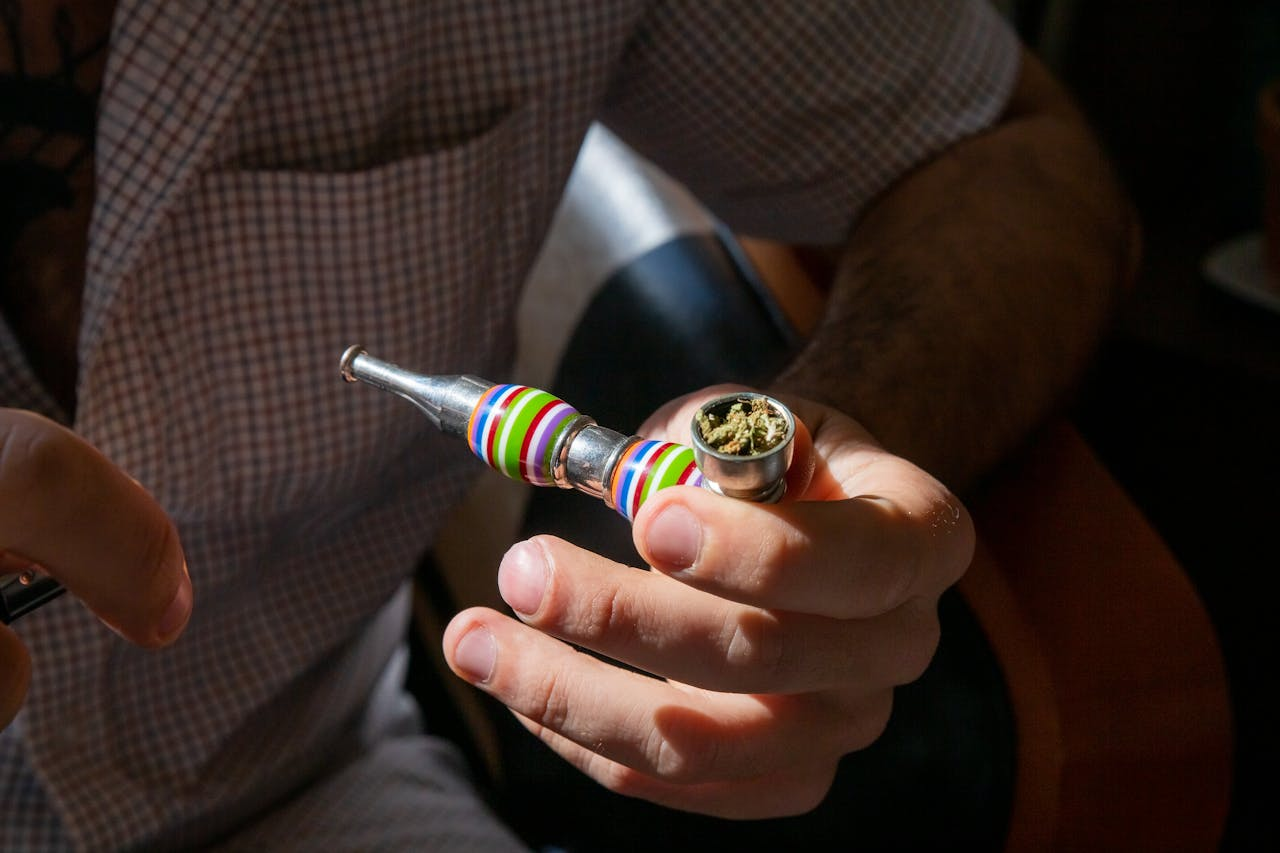 Adult holding a colorful pipe containing cannabis indoors with natural light.